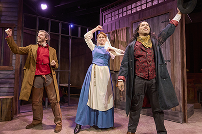 Johnny Blood, wearing a long brown duster, brown chaps, and red vest with his fist up; and a triumphant expression Susana wearing a blue and white novice nun dress with fist swinging and uncertain expression; and Sherrif Green in black duster, burgundy embroidered vest, black pants, and holding up his black brimmed hat with exultant expression. In the bakground are the jail's barred cell and a wood wall with a window and a door.