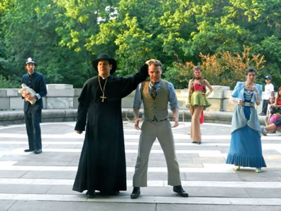 Color photo of the Pinch scene on the monument veranda, with audience sitting on the wall to the right