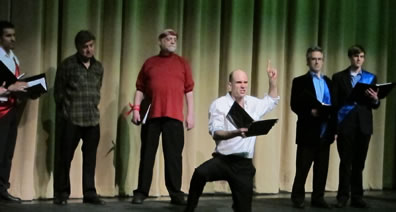 Cast stands with books as Black Prince kneels with finger pointing in air